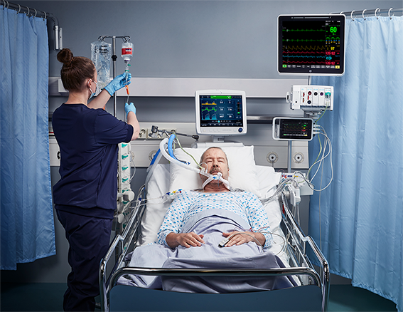 A caregiver is communicating with a patient and working on a GE Healthcare patient monitoring systems.