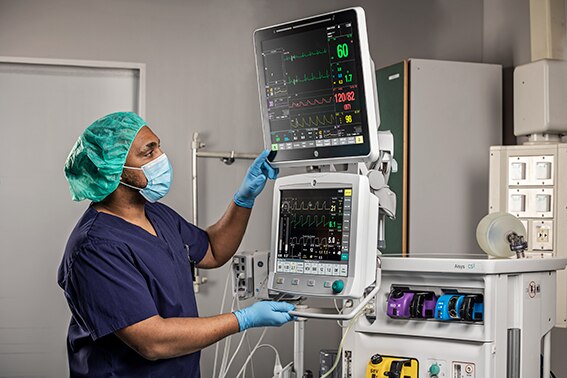 A caregiver is working on a GE Healthcare patient monitoring systems to monitor patient data.